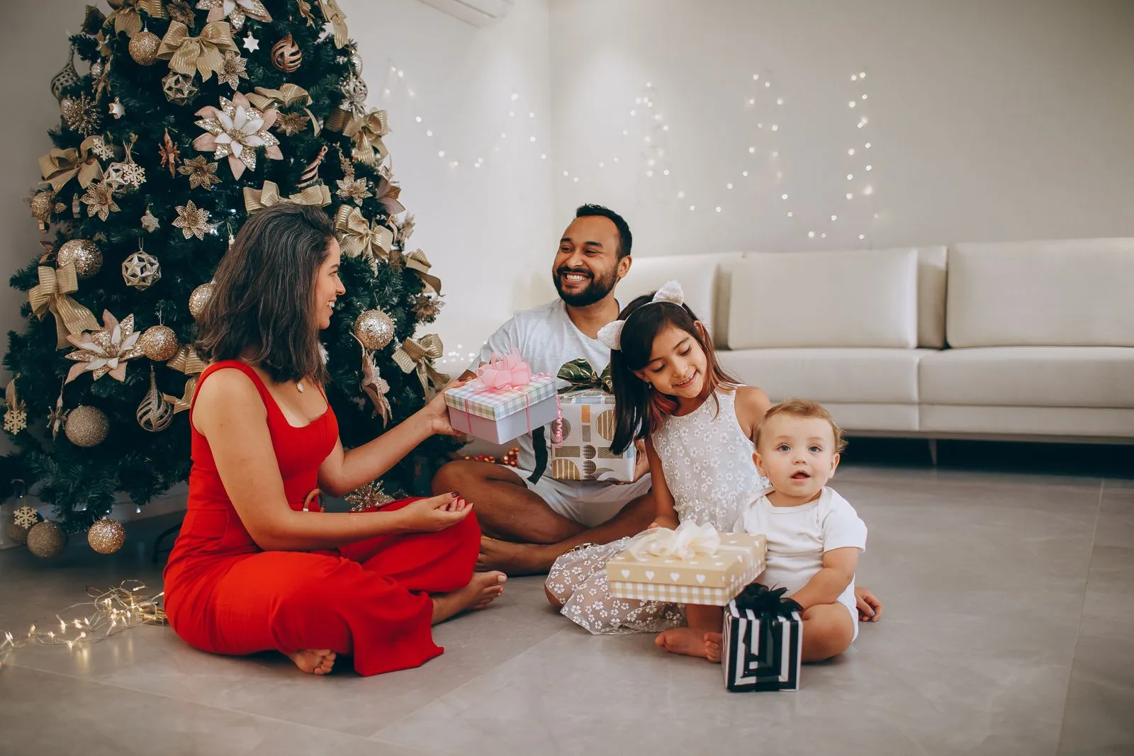 Family enjoying Christmas gift exchange by decorated tree at home.